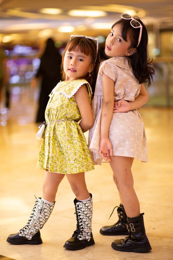 Charming portrait of two young girls posing stylishly indoors in elegant dresses and boots.