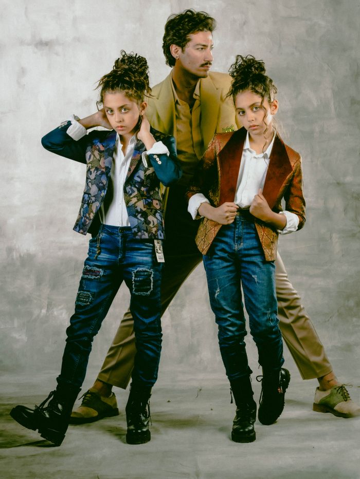 A fashionable family portrait featuring a parent with two stylish children in vintage attire against a textured backdrop.