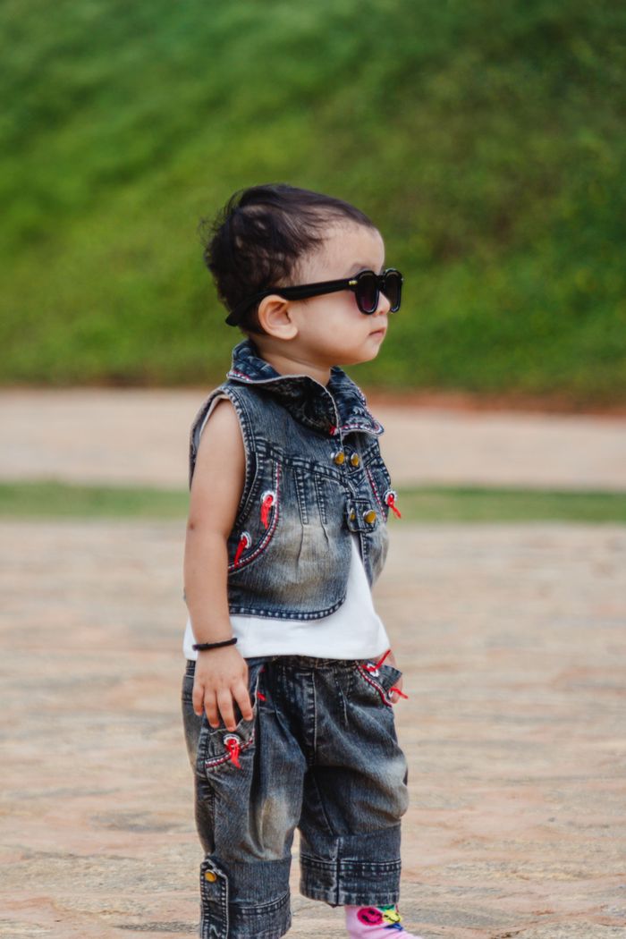 Fashionable baby boy in denim and sunglasses standing outside.