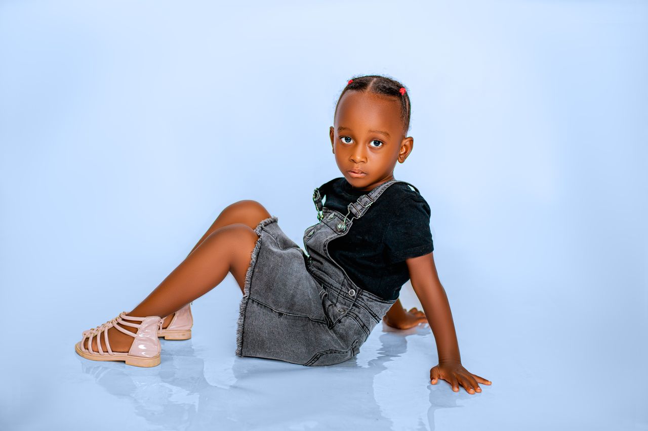 Cute child sitting on a light blue background in stylish casual attire.