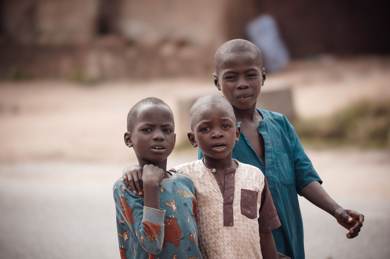 Portrait of three young boys smiling and posing outdoors in Bauchi, Nigeria.