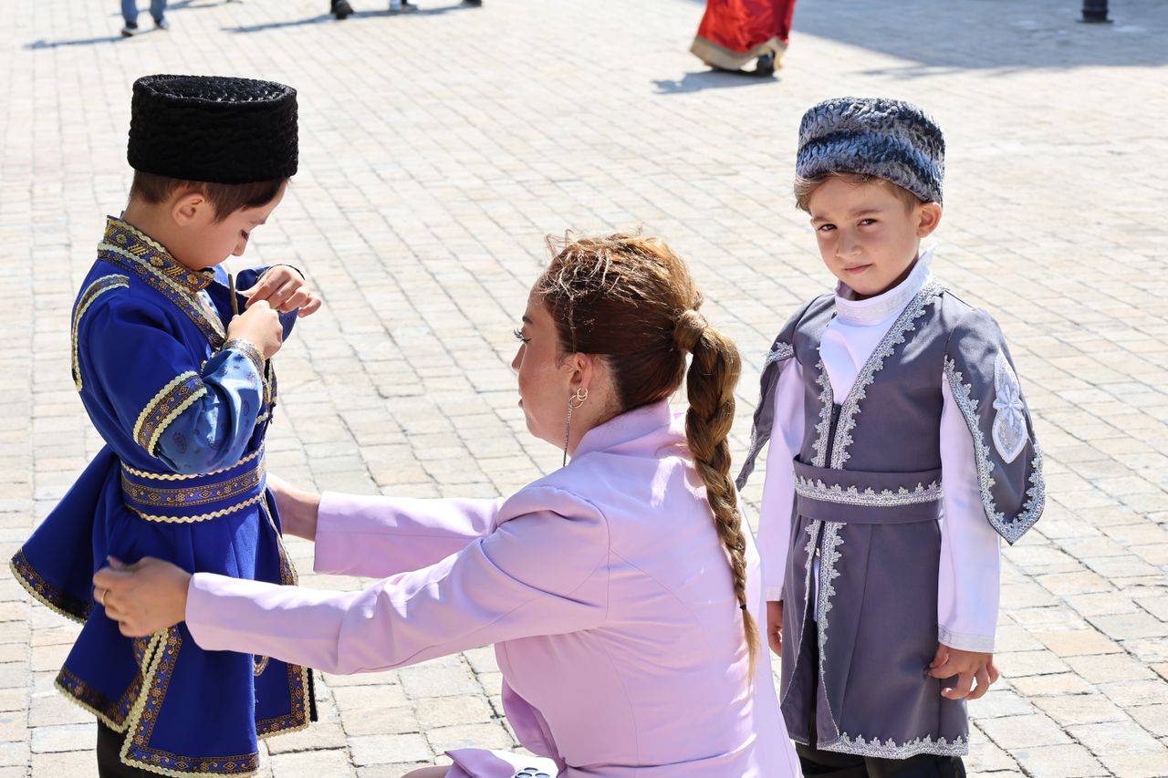 Children in traditional Caucasian costumes prepared for a cultural festival outdoors.