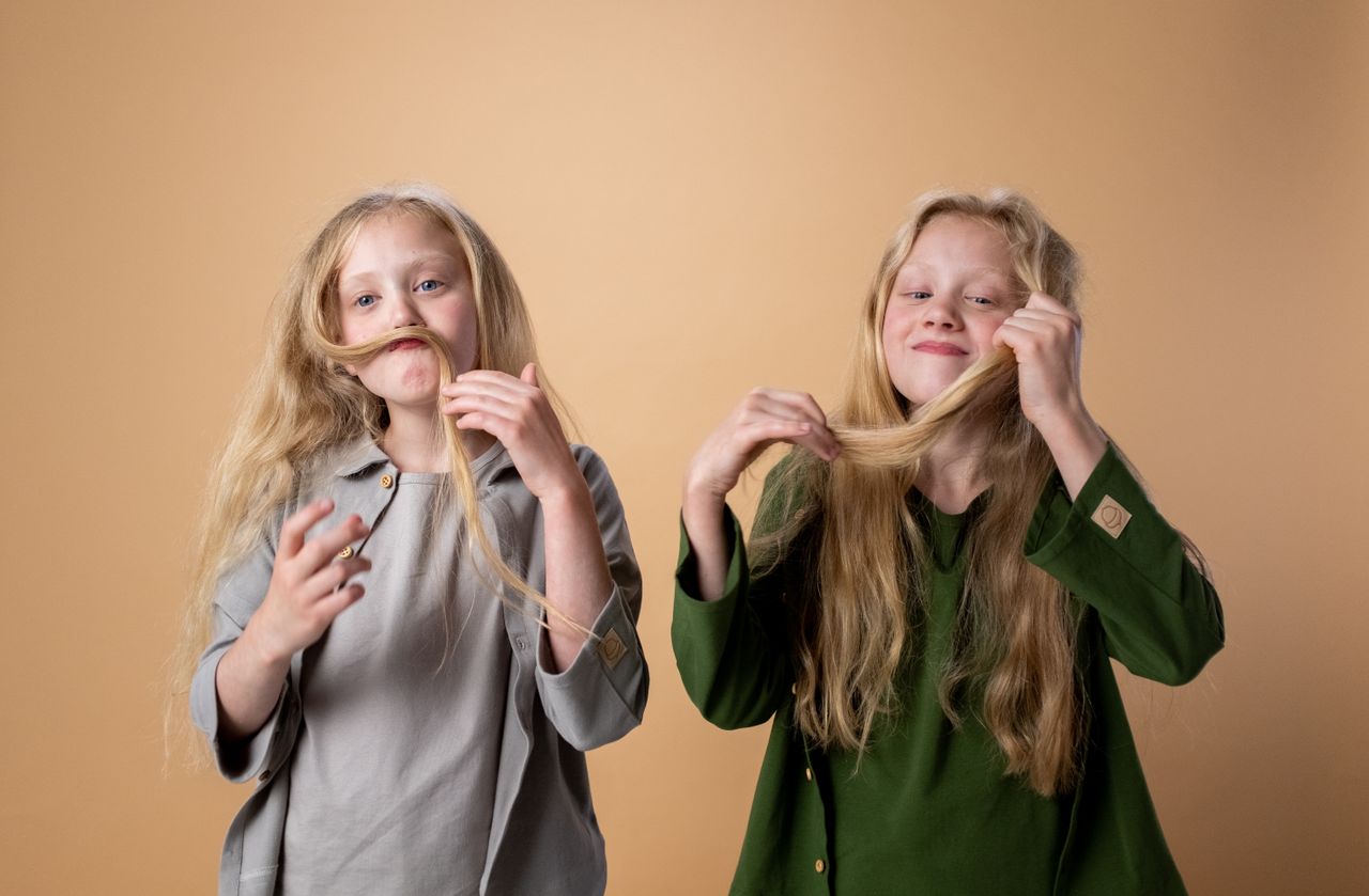 Charming twin girls with long blonde hair making funny faces in a studio setting.